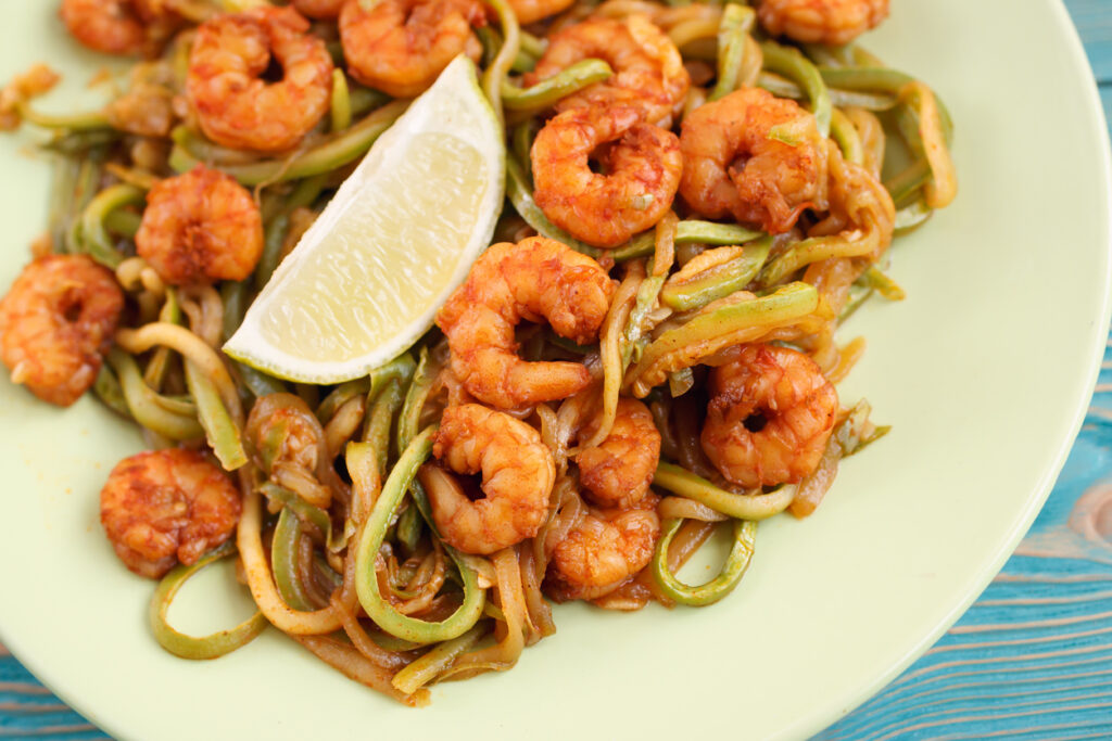 A plate of shrimp and noodles with lemon wedge.