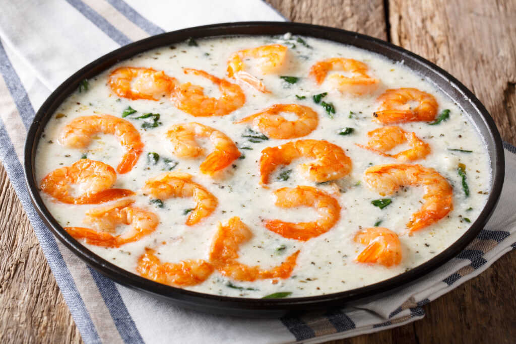 Shrimp with spinach and spices in creamy cheese sauce close-up on a plate on a table. horizontal